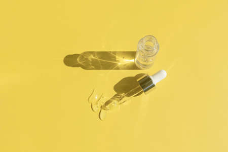 close up of pipette with pouring liquid serum and shadows on yellow backgroundの写真素材