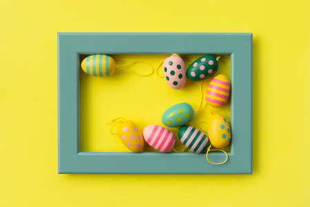 colorful painted easter eggs in a turquoise frame on yellow background festive easter card for your projectの写真素材