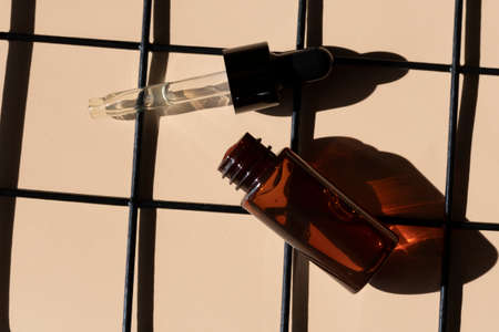 close up of pipette dropper with face serum with bottle and black metal grid on a beige background
