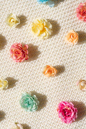 pattern of colorful artificial flowers on a textured beige sweater background for your summer...