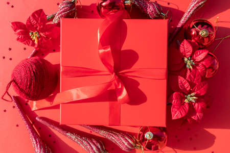 red Christmas gift box with poinsettia and ornaments on a red background for your xmas projectの写真素材