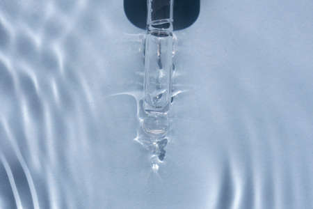 close up of face serum pipette in a fluid with glare on blue background for your beauty projectの写真素材