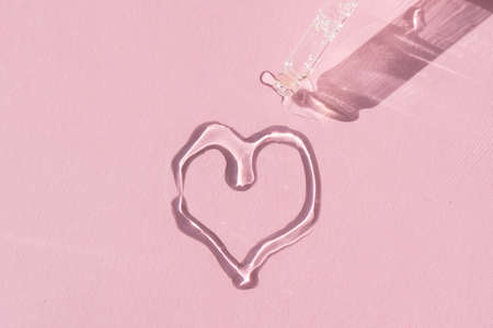 close up of a pipette dropper with pouring face serum in a shape of a heart on a pink background for your beauty projectの写真素材