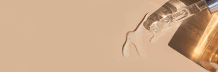 close up of pipette with pouring liquid serum with golden bottle and shadows banner on beige backgroundの写真素材