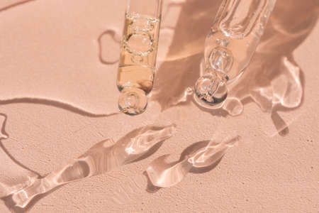 close up of pipette with pouring liquid serum and shadows on beige backgroundの写真素材