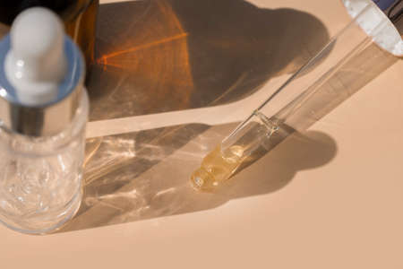 close up of pipette with pouring liquid serum with golden bottle and shadows on beige backgroundの写真素材