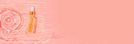 glass container with beauty oil and pipette in pink water with waves and sun glare