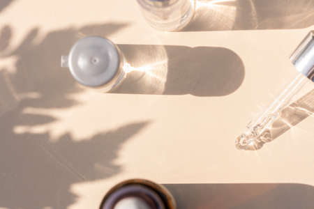 close up of pipette with pouring liquid serum with bottles and graphic shadows with fern plant shadow on beige backgroundの写真素材