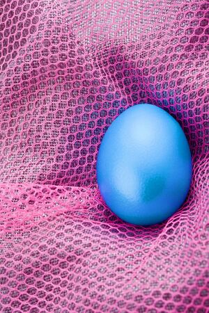 blue easter egg lying on a pink blanketの写真素材