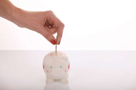 Hand with nail varnish putting coin in piggy bankの写真素材