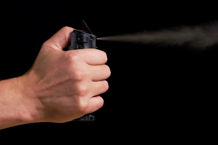 man aiming and spraying pepper spray with visible fog on black backgroundの写真素材