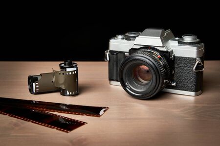 front view of a Classic analog 35 mm camera vintage and analog film rolls on wooden tableの写真素材
