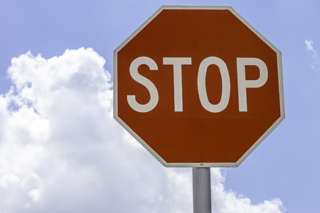 Close shot of a stop sign surrounded by blue sky and clouds の写真素材