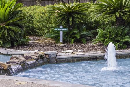 A small waterfall and fountain sitting in front of a No Swimming sign.