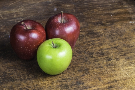A selection of red and green apples sitting on an old piece of wood.