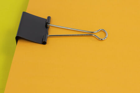 A black binder clip holding together a stack of colorful paper.の写真素材