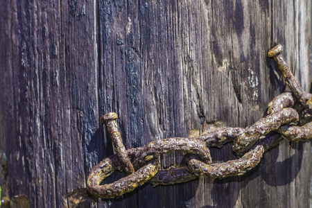 A close shot of an old rusty chain nailed to a wooden pole.