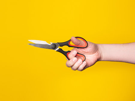 A hand holds a scissor. No face, yellow background.の写真素材