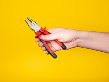 A hand holds a pair of pliers. Yellow background, no face, concept.の写真素材