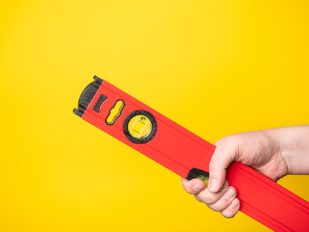 Hand holding a level. Yellow background, no face.の写真素材