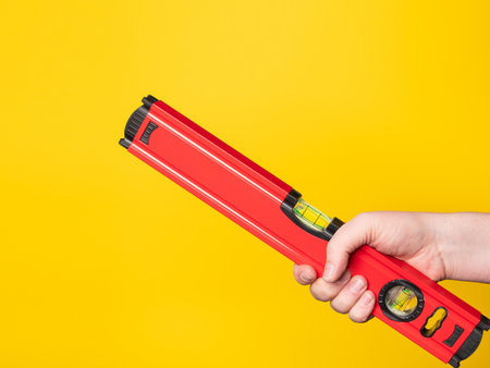 Hand holding a level. Yellow background, no face.の写真素材