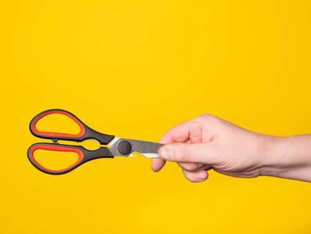 A hand holds a scissor. No face, yellow background.の写真素材