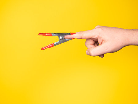 A hand holding a pair of clamps on a yellow background.の写真素材