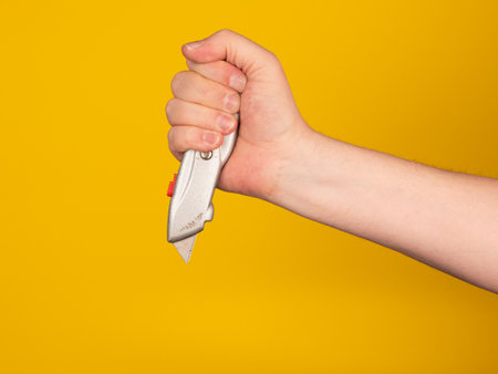 A hand holds a box cutter. No face, yellow background.の写真素材