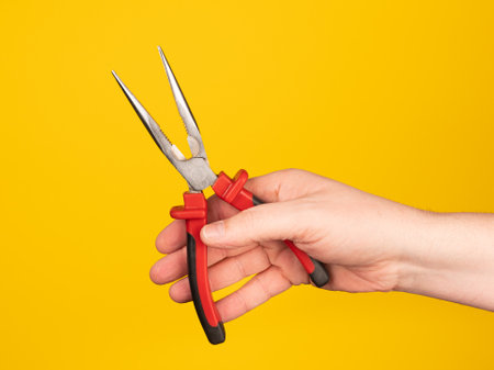 A hand holds a needle nose pliers. No face, yellow background.の写真素材
