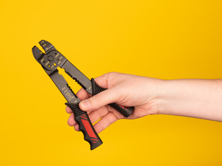 Man's hand holding a pair of crimper on a yellow backgroundの写真素材