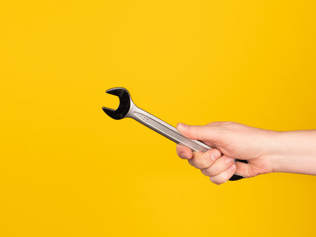 A hand holds an open-end wrench. No face, yellow background.の写真素材