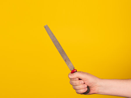 A hand holds a metal file. No face, yellow background.の写真素材