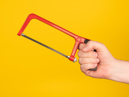A hand holds a metal saw. No face, yellow background.の写真素材