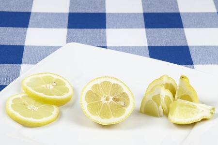 Several lemon pieces and slices on a white porcellain plate. The plate is located on  a blue-white checkered tablecloth.の写真素材