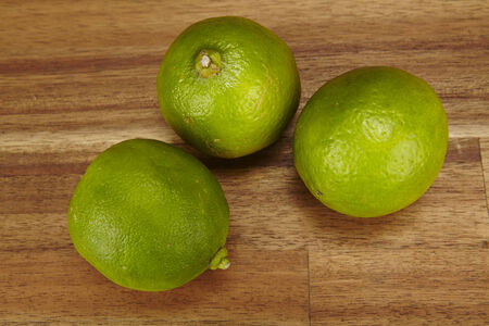 Three green limes are laying on a tabletop of acacia wood.