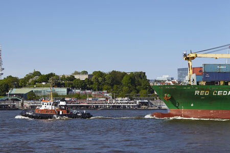The tugboat Bugsier 14 draws the container vessel Red Cedar at Hamburh harbor on May 2014,03.のeditorial素材