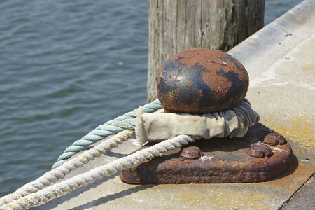 A bollard in a harbor with a thick rope to fasten a ship.の写真素材