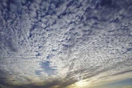 A sky in the evening with many little white and dark clouds and the setting sun.の写真素材