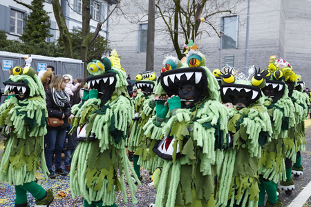 Some fully costumed carnival activists walk through the city during the carnival procession (cortege) of the Carnivel at Basel 2016 (Basle - Switzerland) on February 15, 2016. Some unidentified visitors watching the procession from the edge of the road.のeditorial素材