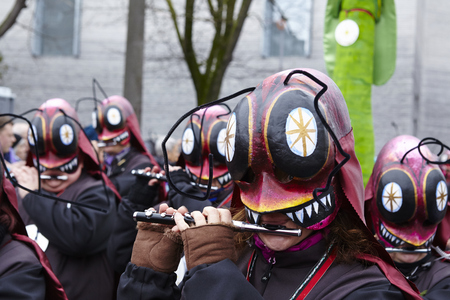 Some fully costumed carnival activists walk through the city during the carnival procession (cortege) of the Carnivel at Basel 2016 (Basle - Switzerland) on February 15, 2016. Some unidentified visitors watching the procession from the edge of the road.のeditorial素材