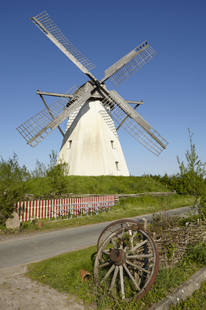 The windmill Grossenheerse (Petershagen) in front of a blue sky is part of the Westphalia Mill Street (Germany). An old wooden cartwheel lays in the foreground.のeditorial素材
