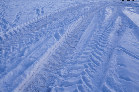 Some skid marks lead into a snowscape at the point of the blue hour in the evening. The snow reflects the light of the blue sky.の写真素材