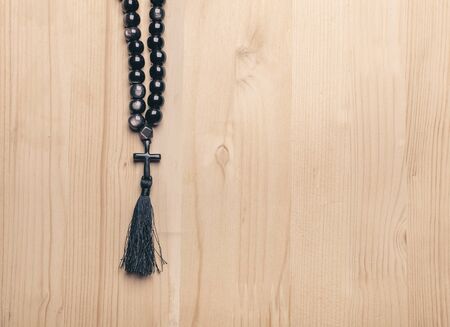 Black stone christianity beads with cross on wooden desk with copy space at right