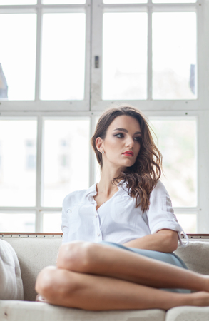young beautiful brunette white woman sitting on sofa in classic interiorの写真素材