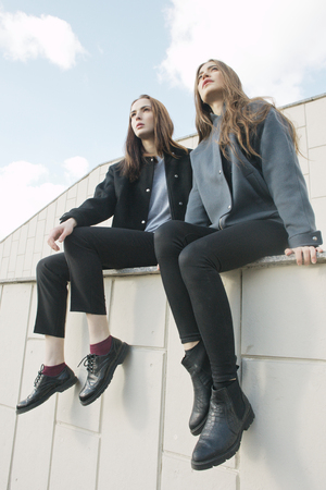 two young fashion woman sit on parapet, low angleの写真素材