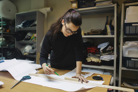 female fashion desighner draws dress template on panel table in workshop interior