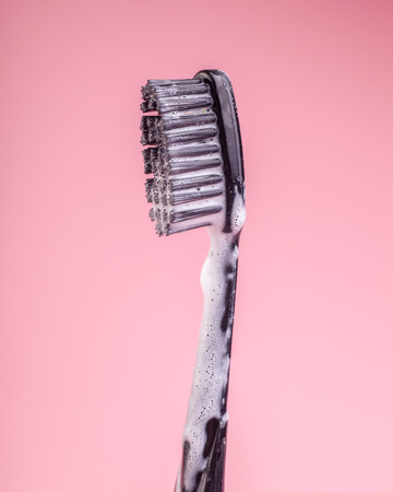 black toothbrush in white toothpaste foam isolated on bright pink backgroundの写真素材