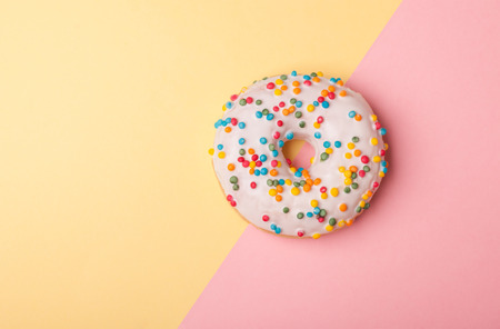 one tasty donut with white glaze isolated on pink-yellow backgroundの写真素材