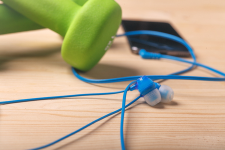 earphones on wooden table with blurred dumbbells and smartphone in background, selective focus,の写真素材