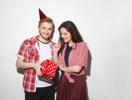 happy young guy with party cap and red gift-box, and his girlfriend isolated on white backgroundの写真素材
